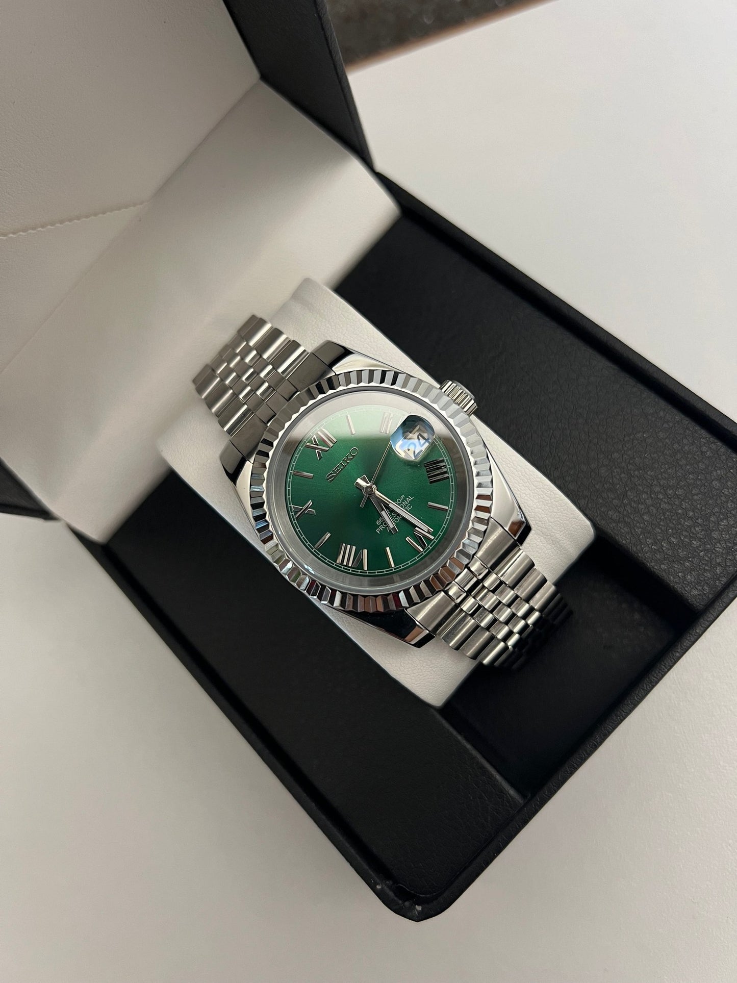 Datejust (Green Roman) Seiko NH35 automatic mod watch. A watch in a box shows a green dial with a silver fluted bezel and a silver jubilee bracelet.