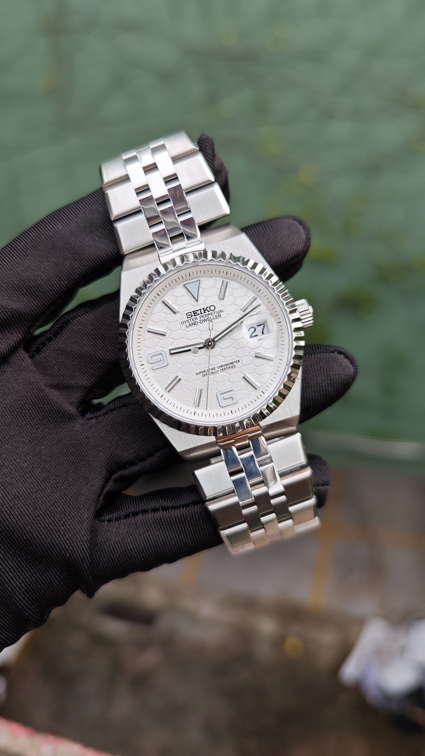 Land-Dweller Seiko NH35 automatic mod watch. A white dial watch with a silver fluted bezel and metal link bracelet held by a gloved hand.