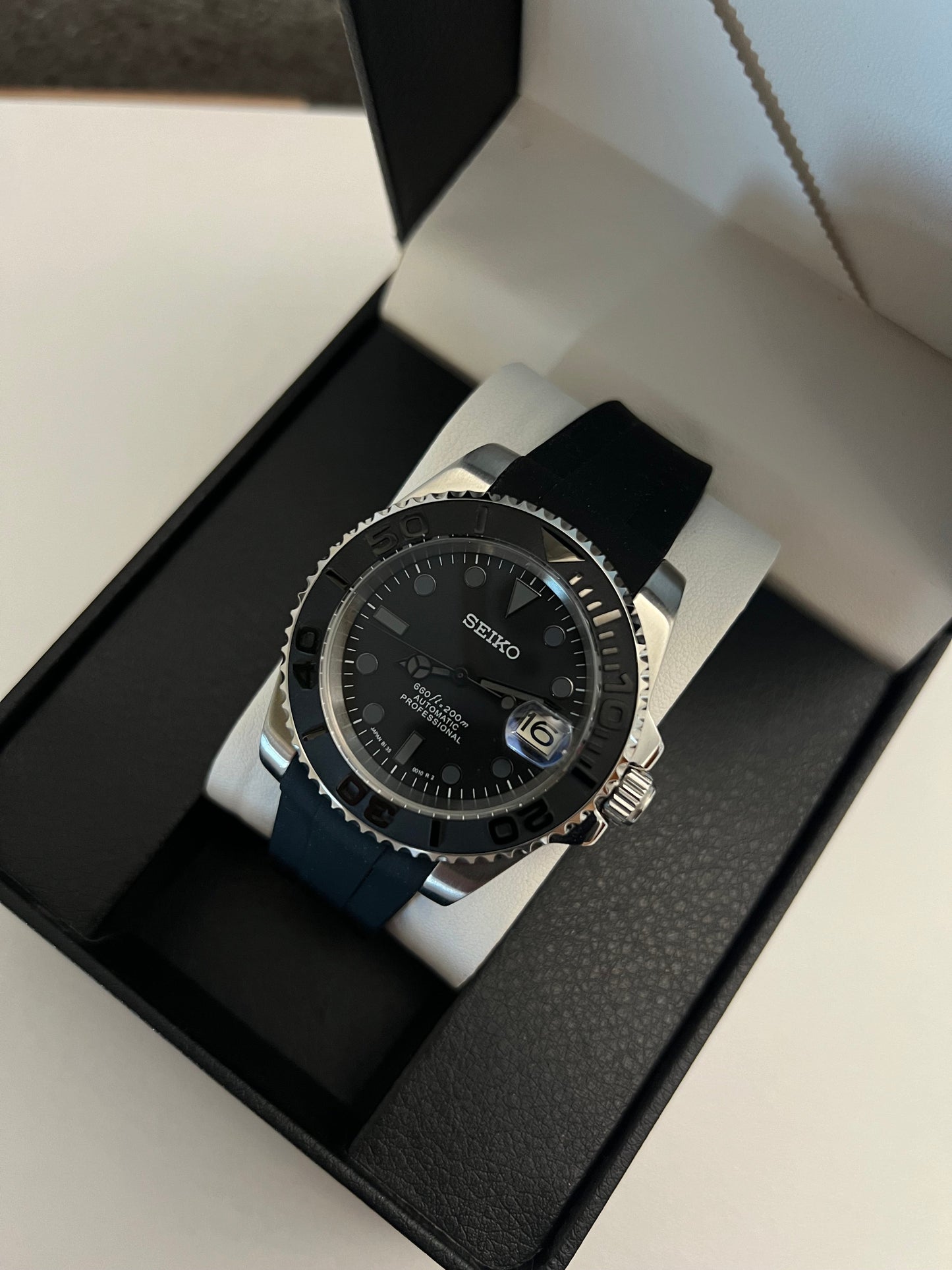 Yacht-Master (Grey) Seiko NH35 automatic mod watch. A full watch with a black dial and bezel on a black rubber strap inside a watch box.