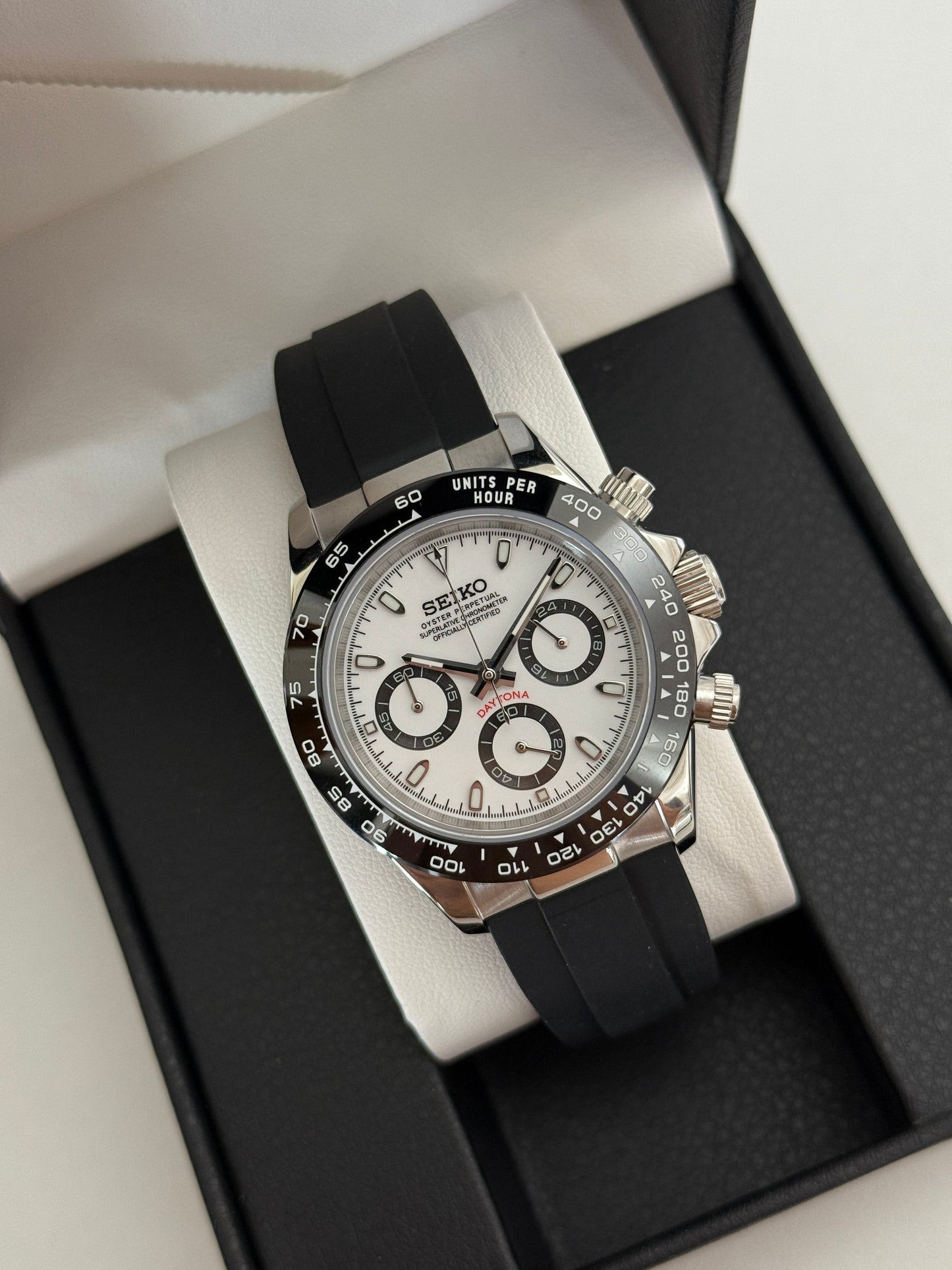 Daytona (Panda) Seiko VK63 meca-quartz chronograph mod watch. A high angle full watch shot in a box showing a white dial with black sub dials and a black bezel.