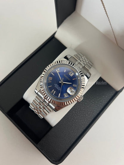Datejust (Royal Blue Roman) Seiko NH35 automatic mod watch. A blue dial watch with a silver fluted bezel and jubilee bracelet shown in a box from a high angle.