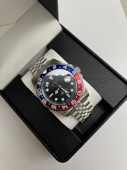 GMT (Pepsi) Seiko NH34 GMT automatic mod watch. A full watch shot inside a box shows a black dial with a blue and red bezel on a silver jubilee bracelet.