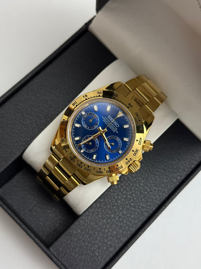 Daytona (Blue Gold) Seiko VK63 meca-quartz chronograph mod watch. A gold tone chronograph watch with a blue dial and gold bezel is shown in a high angle full shot.