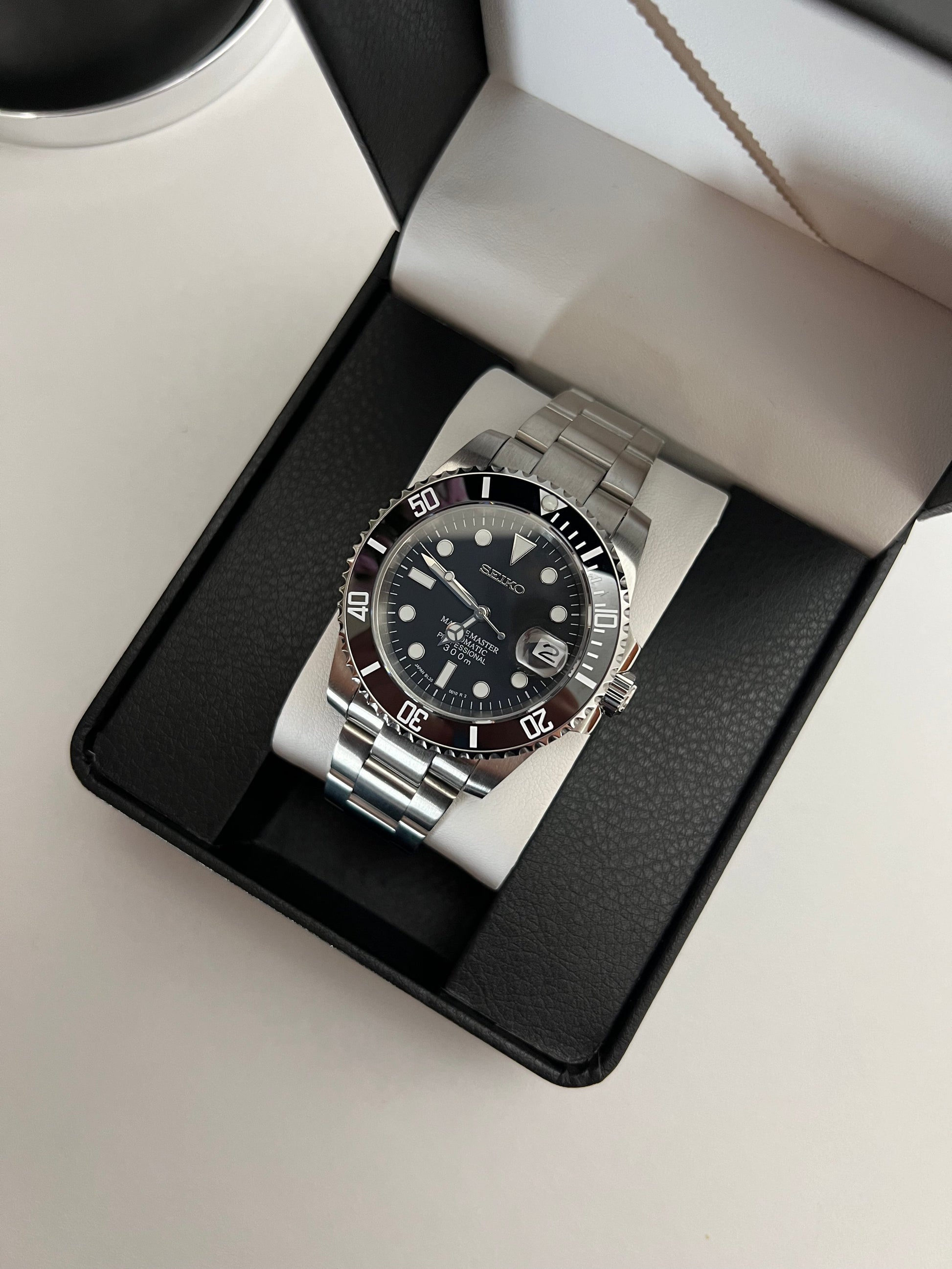 Submariner (Black) Seiko NH35 automatic mod watch. A full watch with a black dial and black bezel on a metal bracelet inside an open black box.