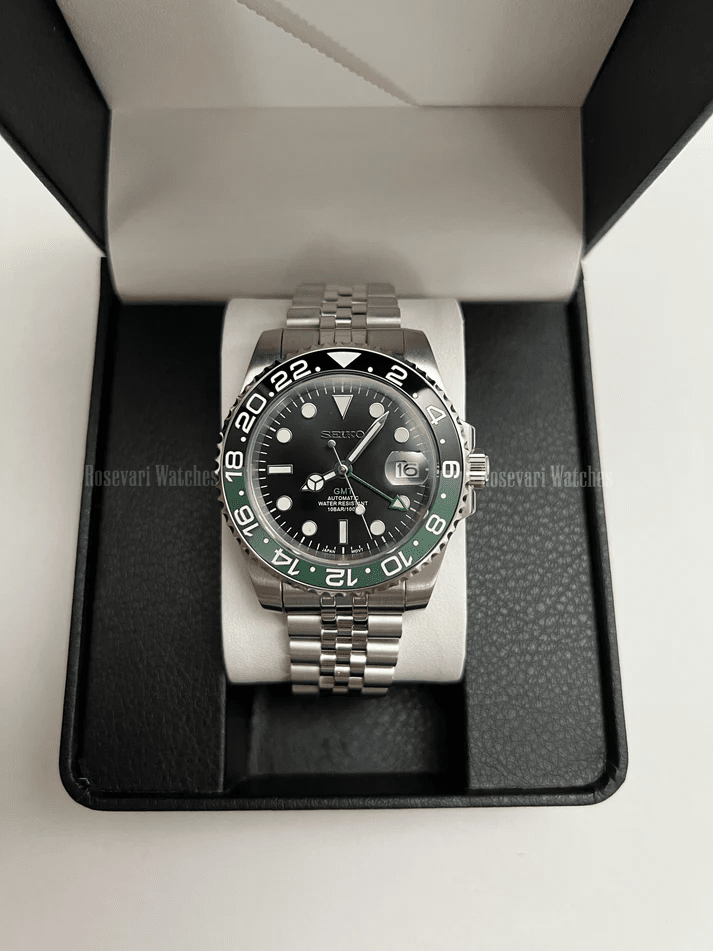 GMT (Sprite) Seiko NH34 GMT automatic mod watch. A full watch with a black dial and a black bezel on a jubilee bracelet inside a watch box.
