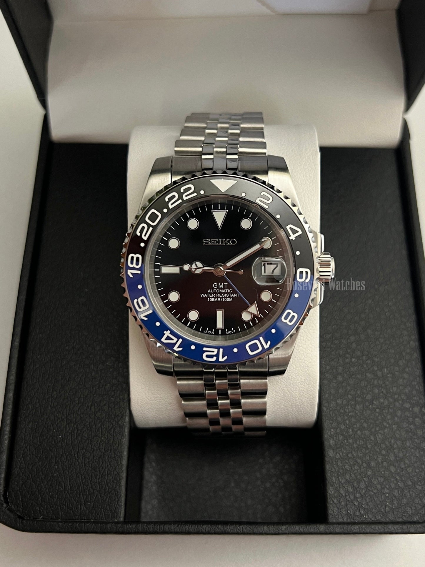 GMT (Batman) Seiko NH34 GMT automatic mod watch. A front view of the watch in a box featuring a black dial and blue and black bezel on a silver bracelet.