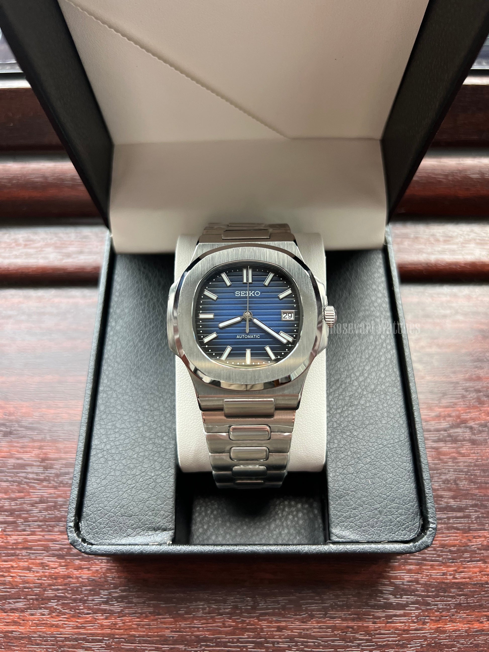 Nautilus (Royal Blue) Seiko NH35 automatic mod watch. A blue dial watch with a silver bezel and metal link bracelet shown in a straight on shot inside a box.