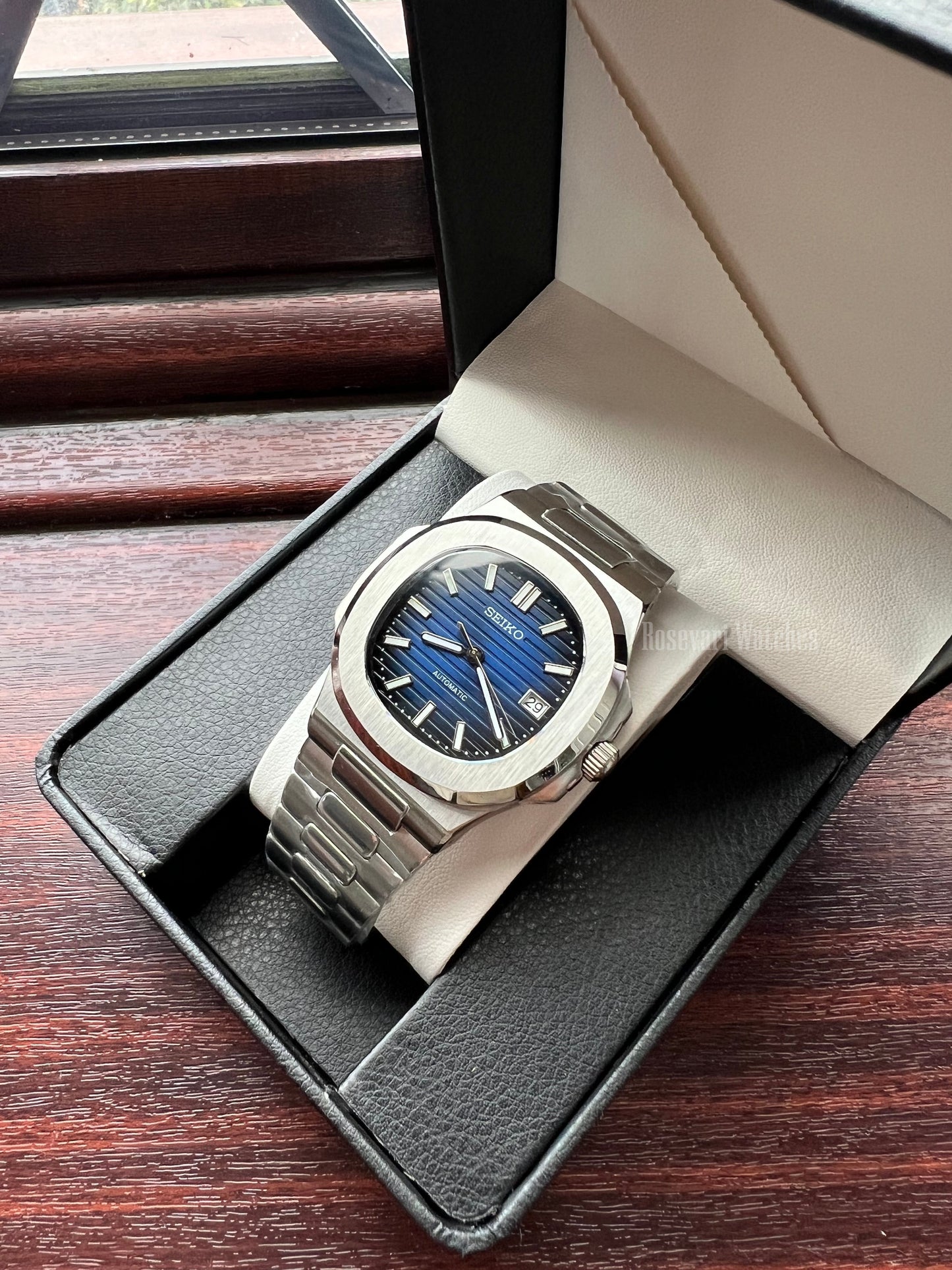 Nautilus (Royal Blue) Seiko NH35 automatic mod watch. A blue dial watch with a silver bezel and metal link bracelet shown in a side angle shot inside a box.