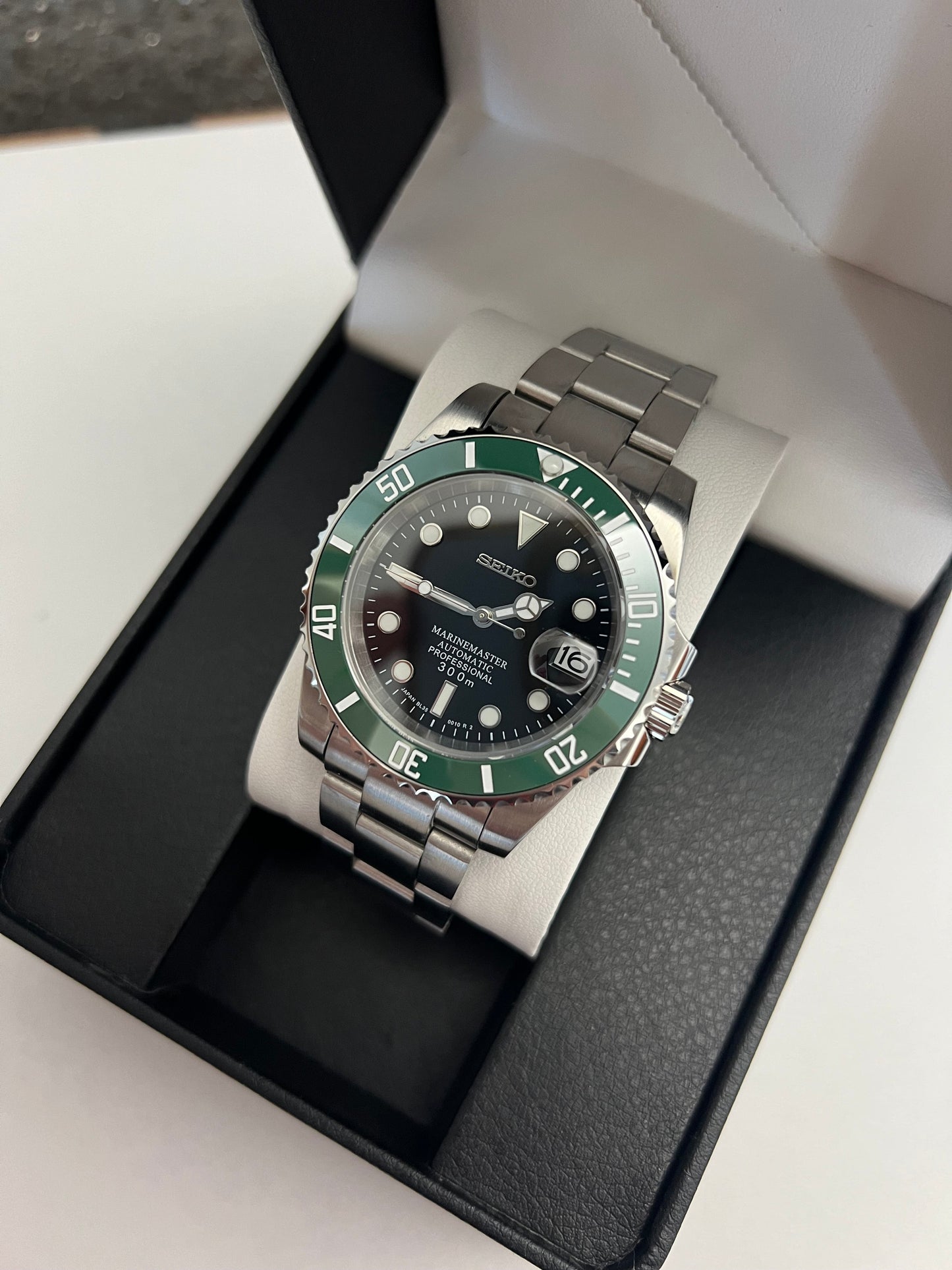 Submariner (Kermit) Seiko NH35 automatic mod watch. A full watch with a black dial and green bezel on a metal link bracelet inside an open watch box.