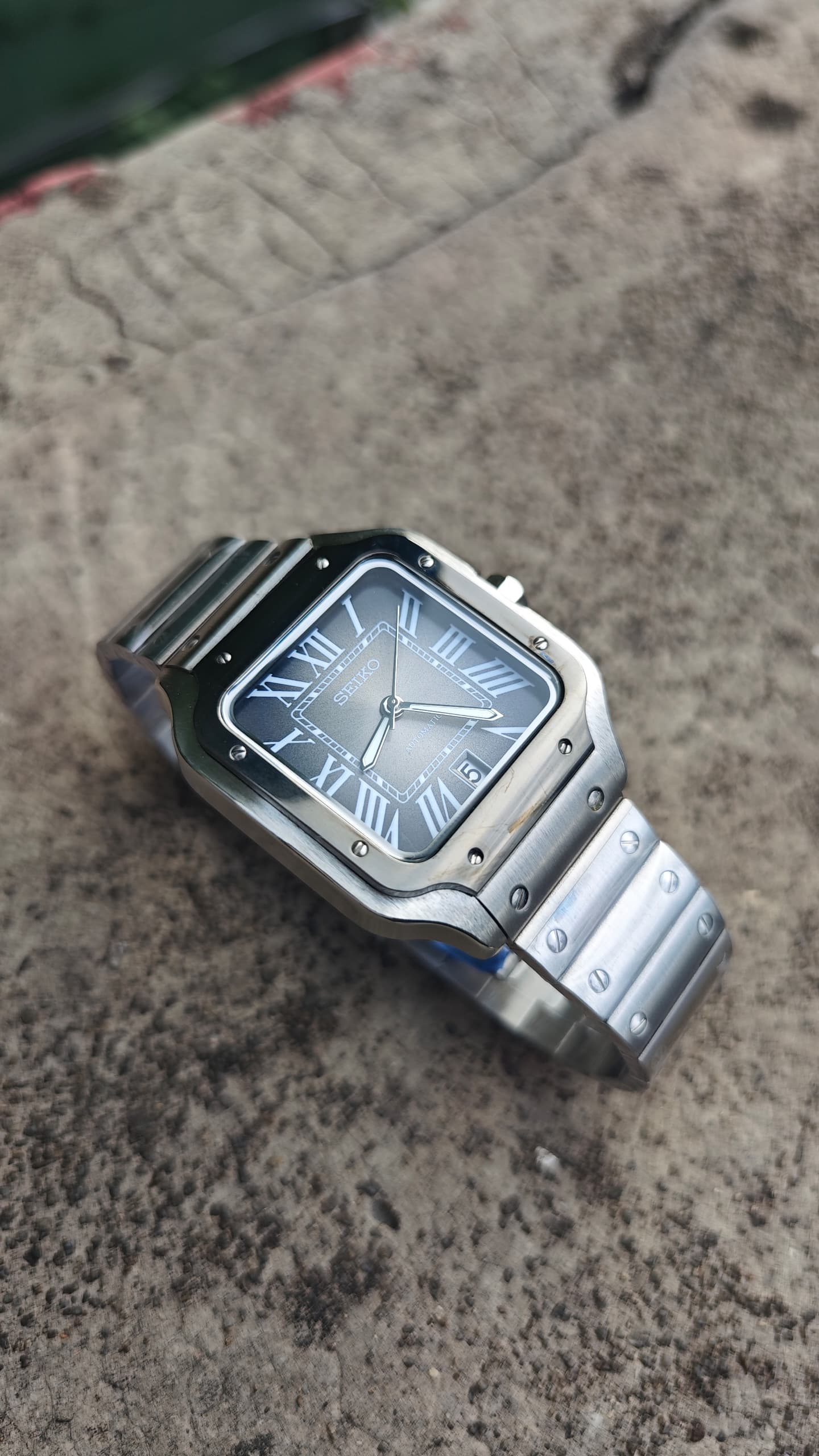 Santos (Graphite) Seiko NH35 automatic mod watch. A side angle full watch shot displaying a grey dial with a black bezel and a metal link bracelet.
