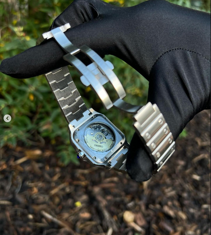 Santos (Emerald Green) Seiko NH35 automatic mod watch. A caseback detail shot showing the mechanical movement and the metal bracelet held by a gloved hand.